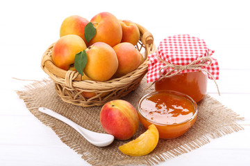Jam in bowl and apricots on white wooden table