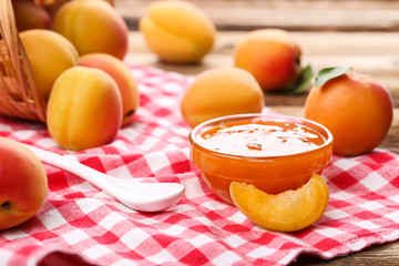 Jam in bowl and apricots on brown wooden table
