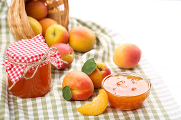 Jam in bowl and apricots on white wooden table