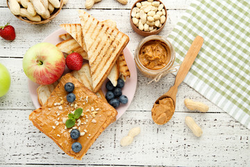 Bread with peanut butter, fruits and nuts on white wooden table