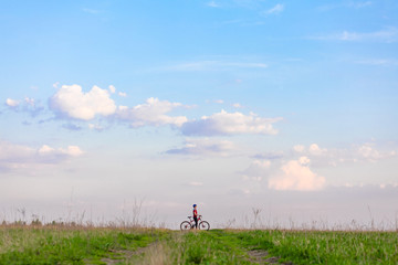 Girl on a bicycle on a background of blue sky and green grass