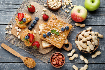 Bread with peanut butter, fruits and nuts on wooden table