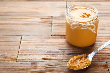 Peanut butter in glass jar with spoon on brown wooden table