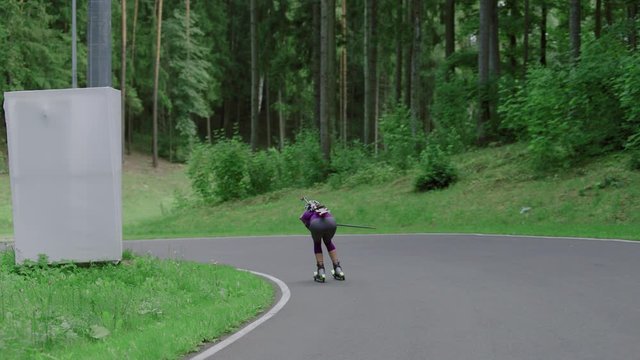 TRACKING Caucasian female professional biathlete roller skiing downhill on a forest track during mid-season practice in summer. ARRI Alexa Mini with Cooke S4 prime lenses RAW graded footage