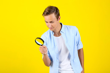 Young man with magnifying glass on yellow background