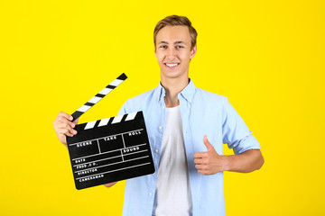 Young man with clapper board on yellow background