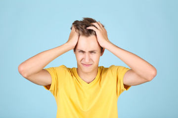 Young man having a headache on blue background