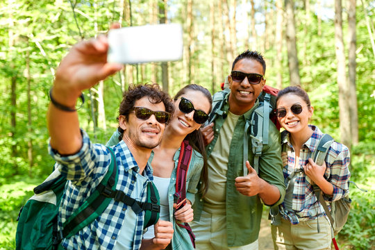travel, tourism, hike and people concept - group of friends with backpacks taking selfie by smartphone in forest - Powered by Adobe