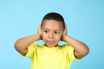 Cute american boy closing ears by hands on blue background