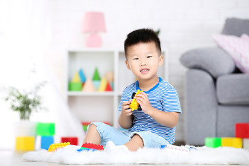 Beautiful boy sitting and playing with plastic toys at home