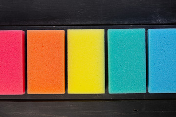 Sponges of different colors in dark background, top view. Five pieces of dishcloth laid in row on dark background, shot from above