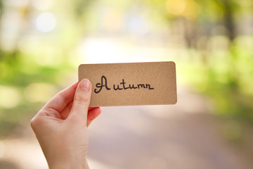 Autumn text on a card.  Girl holding card in autumn park in sunny rays.