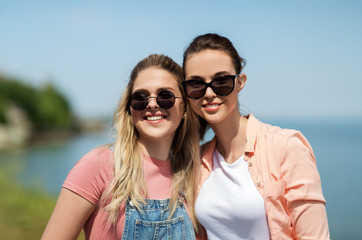leisure and friendship concept - happy smiling teenage girls or best friends in sunglasses at seaside in summer