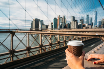 Detail of the hand of a girl holding a glass of coffee while watching New York from a bridge