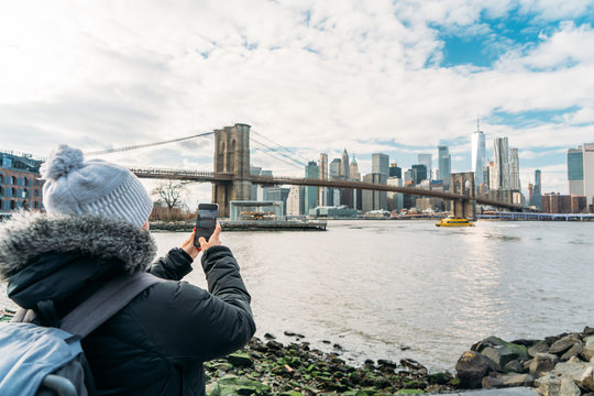 A woman dressed in a coat takes pictures with her cell phone to New York City
