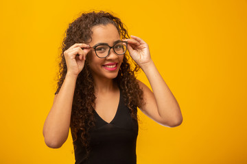 Beautiful young woman with curly hair happy with her glasses. Eye care concept. On yellow background