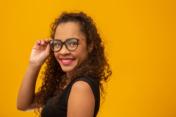 Beautiful young woman with curly hair happy with her glasses. Eye care concept. On yellow background