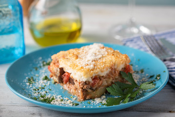greek moussaka on blue plate in white wooden background