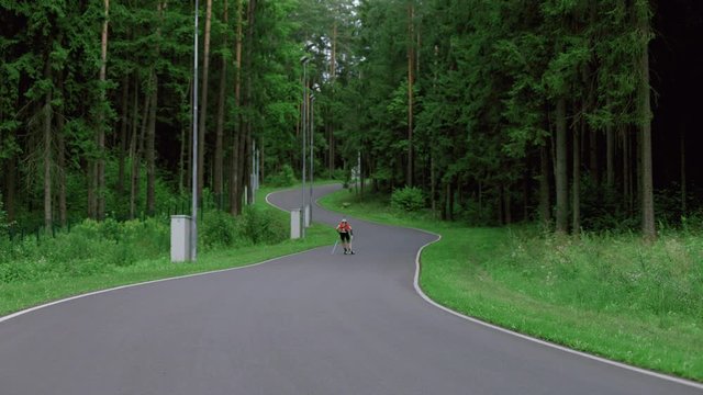 TRACKING Caucasian male professional biathlete roller skiing uphill on a forest track during mid-season practice in summer. ARRI Alexa Mini with Cooke S4 prime lenses RAW graded footage