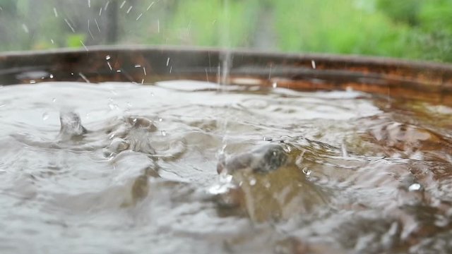Drops and splashes of rainwater fall from the roof into a metal barrel during rain 