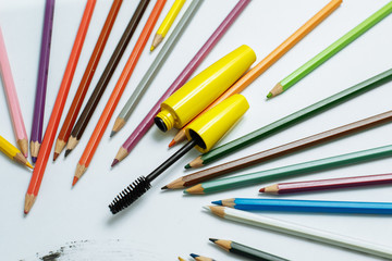 yellow mascara among pencils on a white background