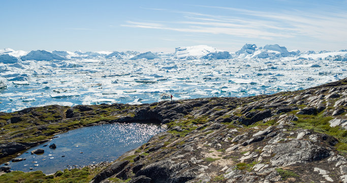 Travel in arctic landscape nature with icebergs - Greenland tourist man explorer - tourist person looking at amazing view of Greenland icefjord - aerial image. Man by ice and iceberg in Ilulissat.