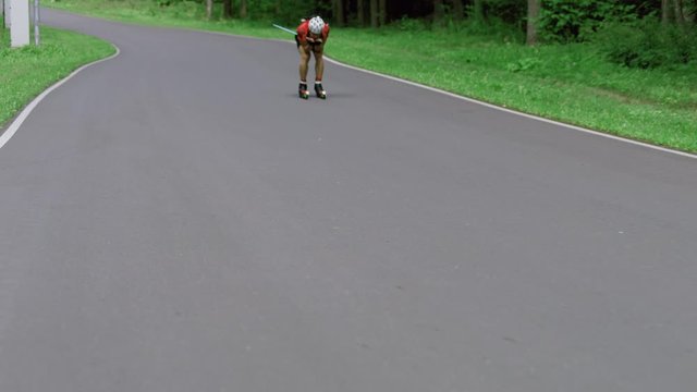TRACKING Caucasian male professional biathlete roller skiing downhill on a forest track during mid-season practice in summer. ARRI Alexa Mini with Cooke S4 prime lenses RAW graded footage