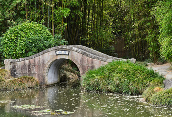 Fototapeta na wymiar Asian Arched Bridge over Garden Creek with Bamboo Background