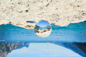 Obraz premium Lake Garda (Lago di Garda or Lago Benaco) seen through a glass crystal ball placed on rock. Selective focus