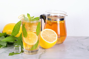 Glass of iced tea with mint and lemon on marble table. Cold drink.