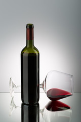 Glasses of red wine lying on mirror surface and bottle of red wine