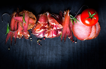 A set of different types of raw smoked meat. Jamon Lomo, сoppa and fillet on a black background.