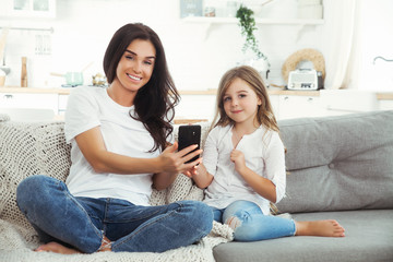 Obraz premium Smiling mother and little daughter playing games with smartphone