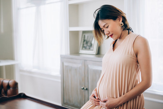 24 Weeks pregnant woman relaxing near window at home in living room
