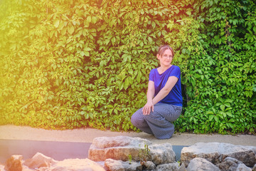 Girl on the wall background of green leaves, copy space. A stone floor, a wall of creeper and a...