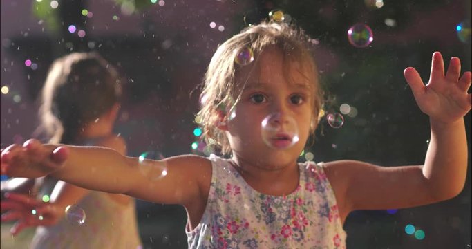 Authentic shot of two cute little girls having fun playing with soap bubbles outside their house on a sunny day.