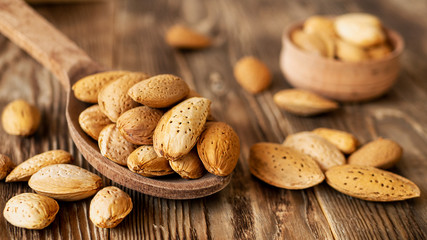 Almonds in wooden spoon on a brown rustic background