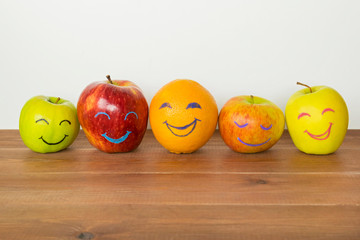 Different apples and orange with funny faces, tolerance, originality or friendship concept.