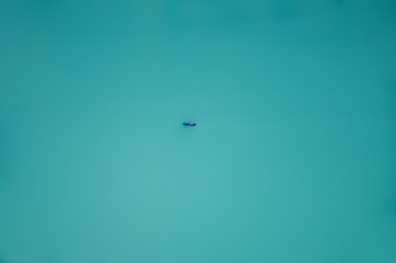 Lone boat sailing at turquoise Oeschinensee in Switzerland. Swiss Oeschinen Lake. Aerial view, blurred boat. Minimalist nature, escape, lost concept. Conceptual, abstract