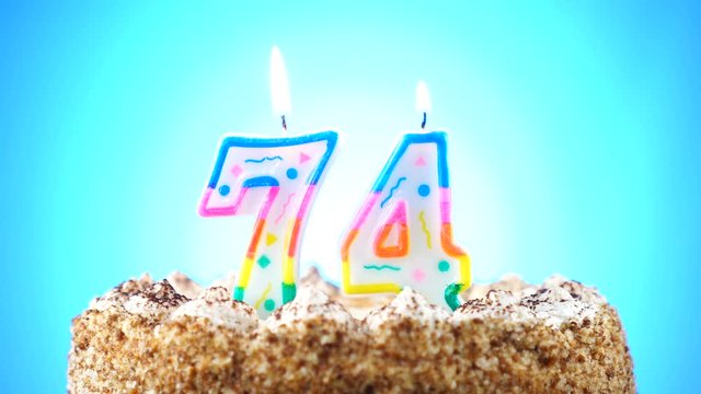 Birthday cake with a burning birthday candle. Number 74. Background changes color