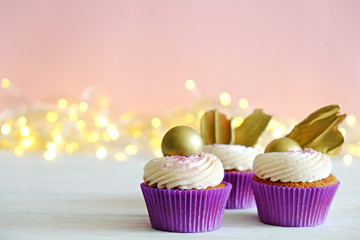 Sweet organic cupcake in purple wrap with cream cheese frosting swirl and golden chocolate decoration on white wooden textured table. Close up, copy space, background.