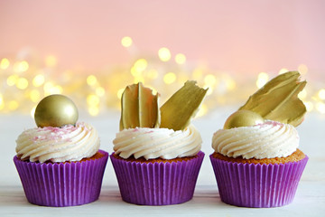 Sweet organic cupcake in purple wrap with cream cheese frosting swirl and golden chocolate decoration on white wooden textured table. Close up, copy space, background.