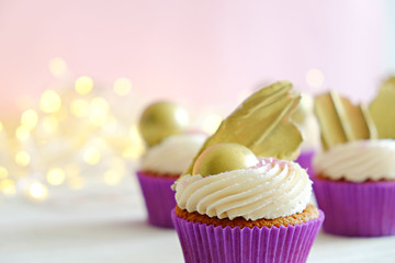 Sweet organic cupcake in purple wrap with cream cheese frosting swirl and golden chocolate decoration on white wooden textured table. Close up, copy space, background.