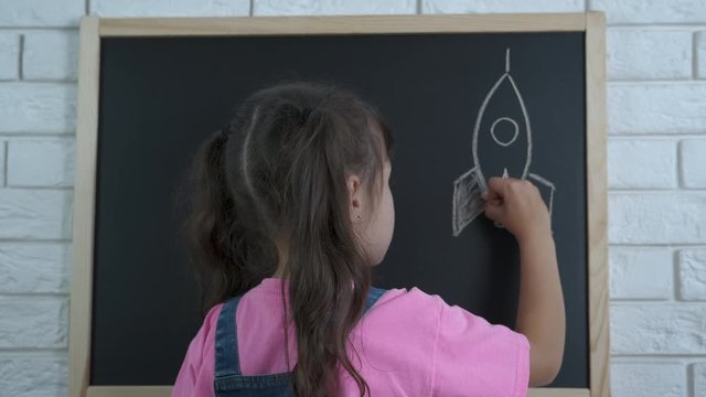 Child draw a space. Little girl draws a spaceship.