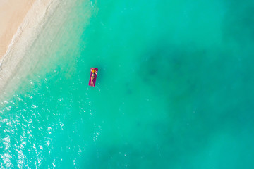 Aerial view of slim woman swimming on the swim mattress in the transparent turquoise sea. Summer seascape with girl, beautiful waves, colorful water. Top view from drone