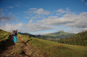 Obraz premium Man standing on the dirt road with hiking backpack and sticks in the background of tree covered hills