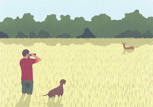 A man with binoculars and dog standing in field looking at wild deer