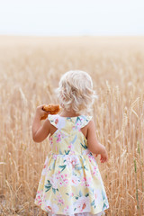 Children with croissant. Child holding croissant in hands. Summer. Adorable  little girl in the wheat field on summer day. Portrait of handsome blond girl  at summer time, in the wheat field