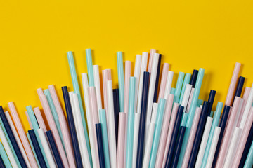 Multicolored plastic cocktail tubes straws on yellow background