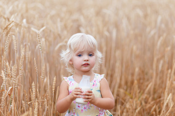 Happy child holding milk iin hands.Beautiful portrait of a young child in a field. Children with milk.  Happy child holding bread in hands. Little girl in cereal field.